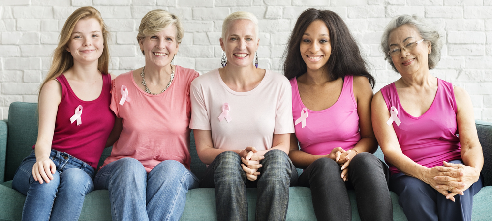 Smiling women sitting on couch with breast cancer awareness ribbons